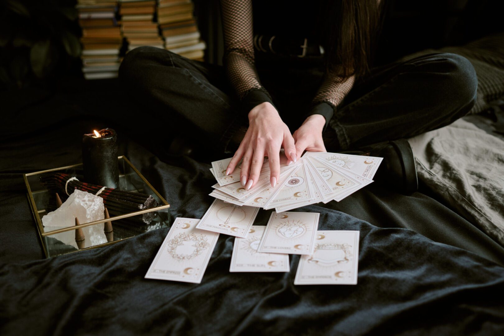 Medium close up of unrecognizable female hands holding and touching tarot cards while black candle burning on tray