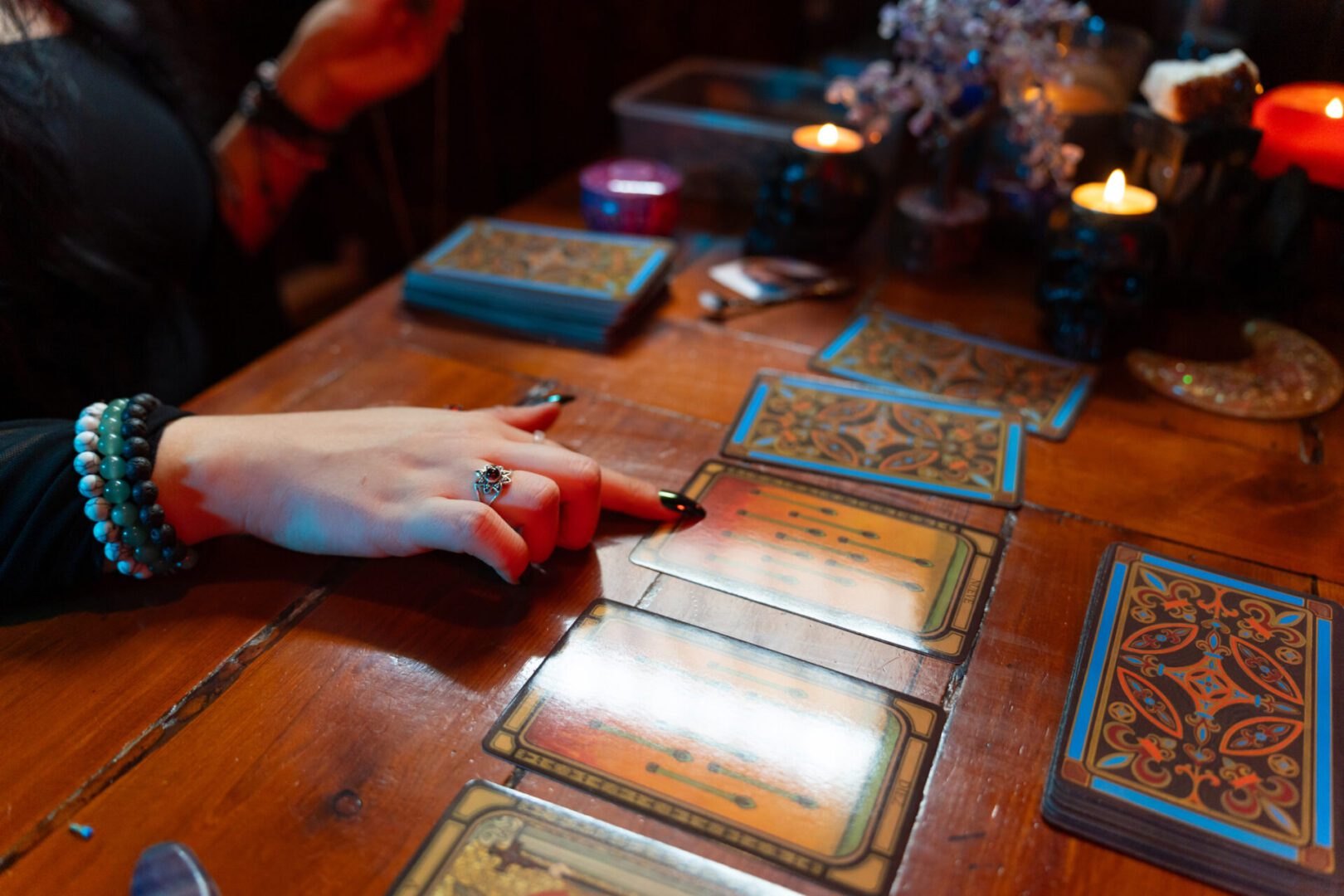 Fortune teller pointing at tarot cards spread on a wooden table, predicting future during mystical session with candles